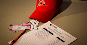 A Carolina Hurricane's hat is on a table with printed tickets and a silent auction sheet. The sheet has several names and bids already on it.